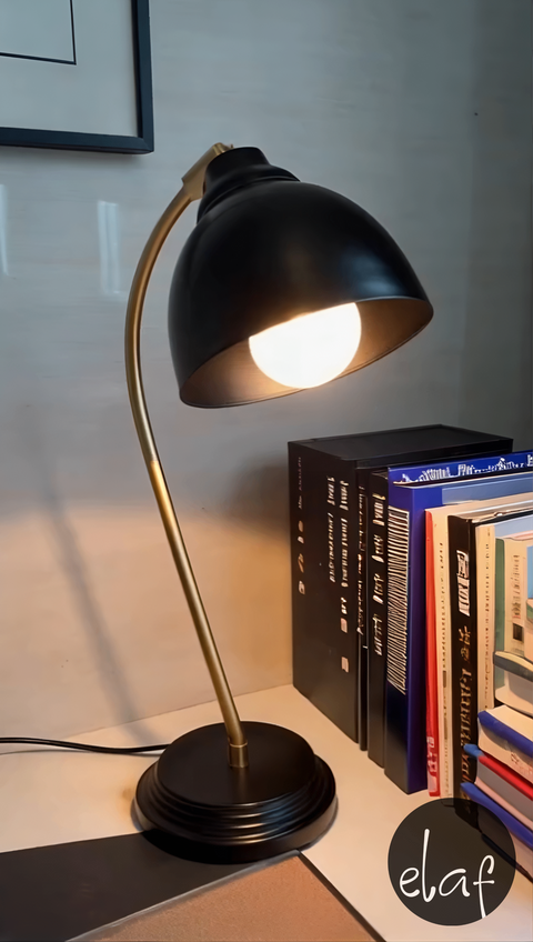 Black and gold vintage desk lamp with curved arm and adjustable black metal head, styled on a modern desk with books
