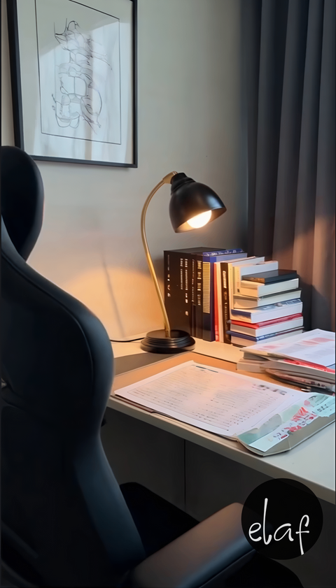 Black and gold vintage desk lamp with curved arm and adjustable black metal head, styled on a modern desk with books