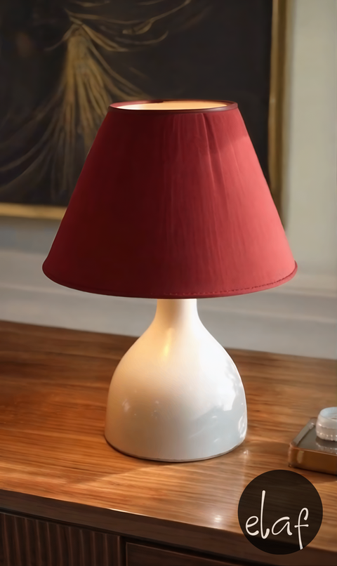 A maroon and off-white table lamp with a fabric shade and metal base, placed on a wooden surface.
