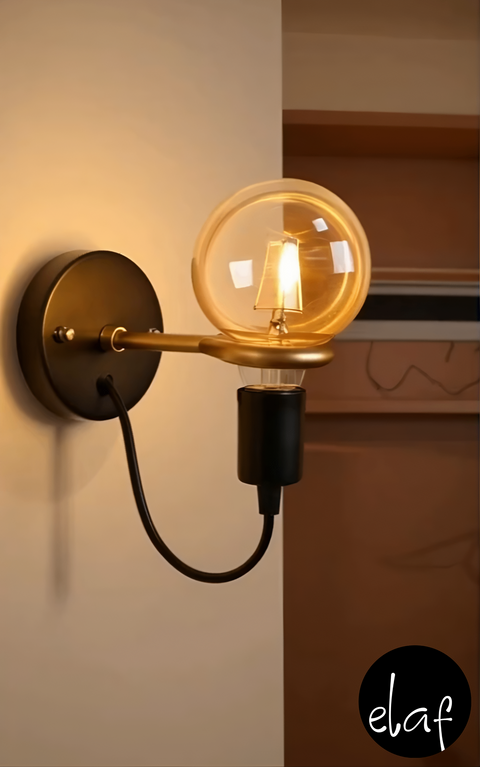 Modern wall sconce with matte black base and gold arm, exposed globe bulb and black cord mounted on wall