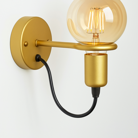 Gold wall sconce with round brushed base and clear globe bulb, minimalist lighting design with black cord on neutral wall