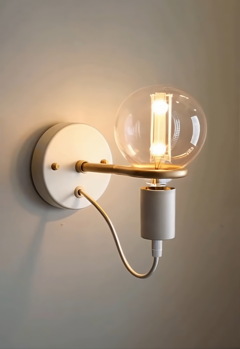 White and gold wall sconce with round base and exposed globe bulb, mounted on light-colored wall for soft modern lighting